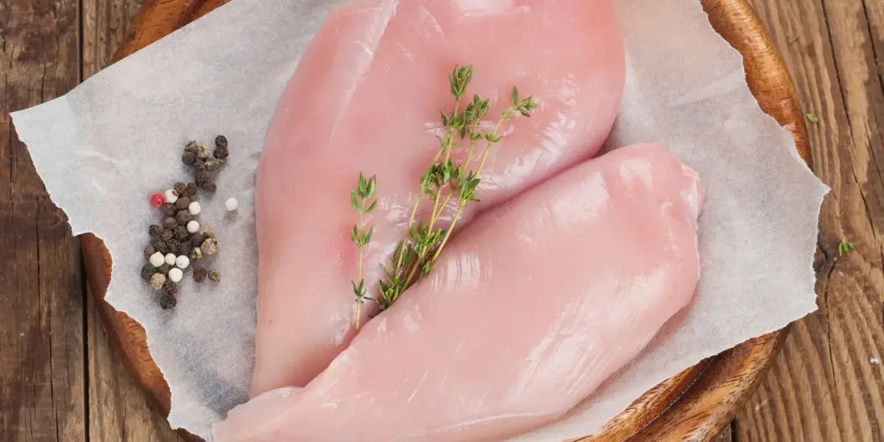 Due petti di pollo crudi, freschi e succulenti, adagiati su carta forno con pepe misto e rametti di timo.