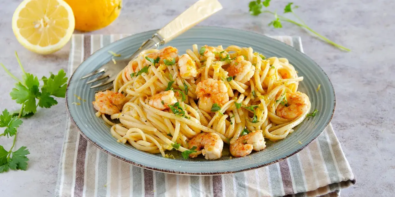 Un piatto di pasta con gamberetti, condita con limone e prezzemolo, accompagnata da limoni freschi e parmigiano.
