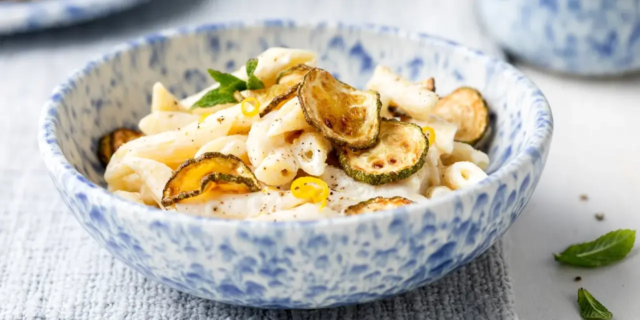 Piatto di pasta cremosa con ricotta e zucchine croccanti, guarnito con scorza di limone e menta.