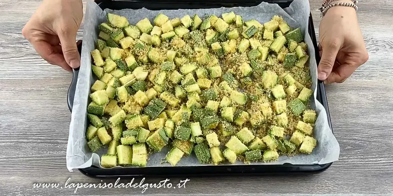 Zucchine gratinate al forno pronte per essere infornate, tagliate a cubetti e cosparse di pangrattato.