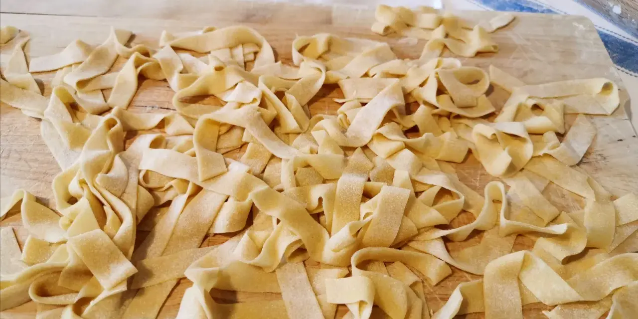 Fettuccine fresche, tagliatelle fatte in casa sparse su un tagliere di legno, pronte per essere cucinate.