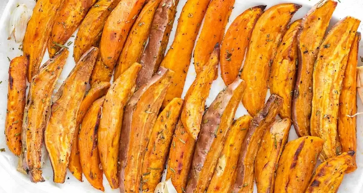Patate dolci al forno, tagliate a spicchi e condite con erbe aromatiche, servite su un piatto bianco.