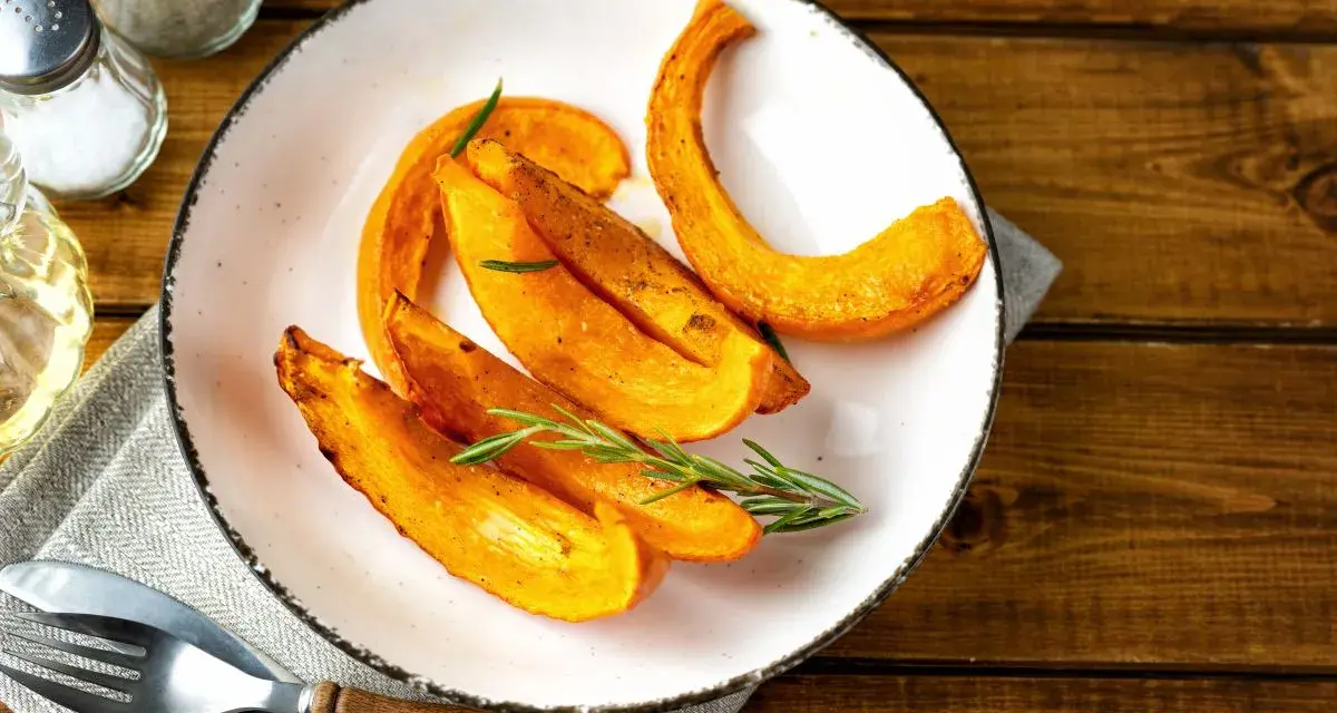 Fette di zucca al forno dorate e profumate, guarnite con rosmarino fresco, pronte per essere gustate.