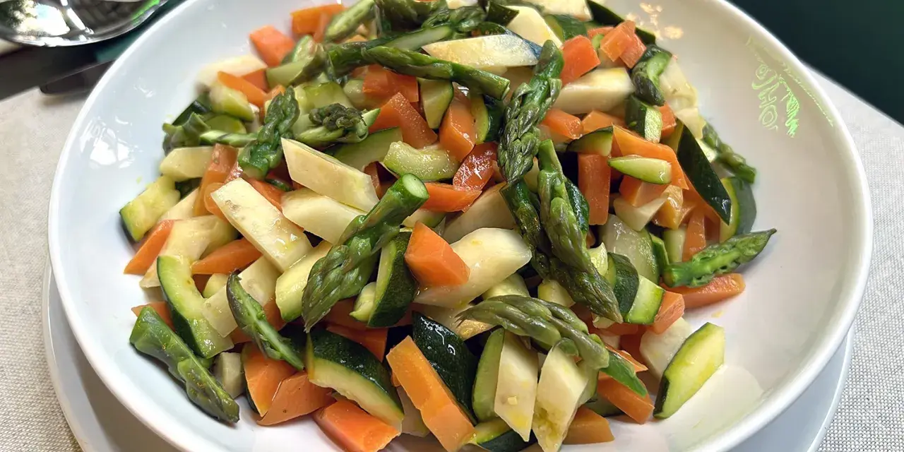 Un piatto invitante di verdure in padella: carote, zucchine e asparagi tagliati a pezzetti, cotti al punto giusto.