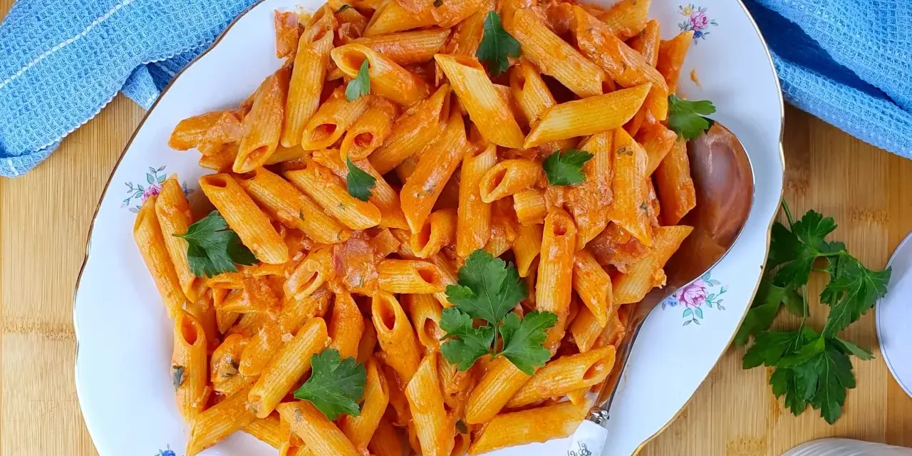 Piatto di penne al baffo cremose, guarnite con prezzemolo fresco, pronte per essere gustate.