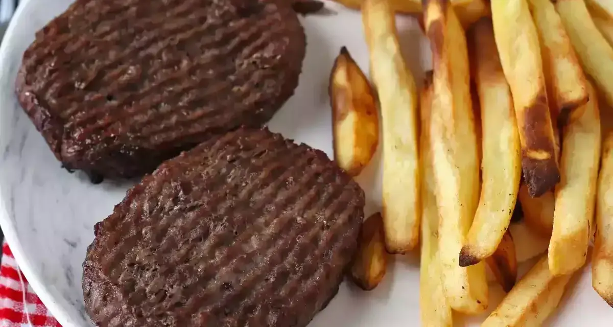 Due hamburger in friggitrice ad aria con patatine fritte dorate su un piatto bianco.