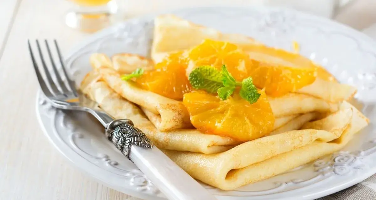 Deliziose crepes senza uova, guarnite con spicchi d'arancia succosa e foglioline di menta fresca. Un piatto leggero e gustoso.