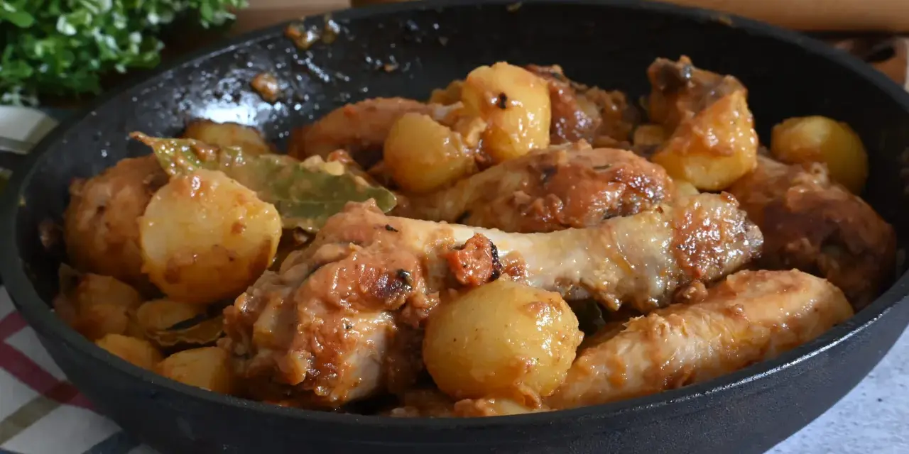 Un saporito pollo in umido con patate e alloro, cotto in una padella di ghisa, pronto per essere gustato.
