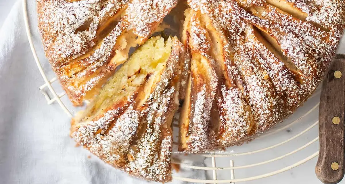 Deliziosa torta di mele in friggitrice ad aria, spolverata di zucchero a velo, con una fetta tagliata per mostrare il morbido interno.