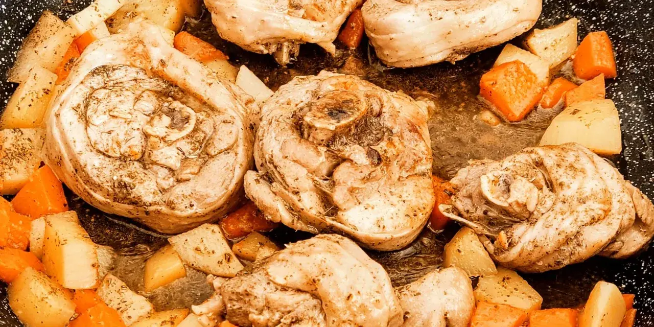 Porzioni di ossobuco di tacchino cotte in padella con patate e carote a cubetti, condite con erbe aromatiche.