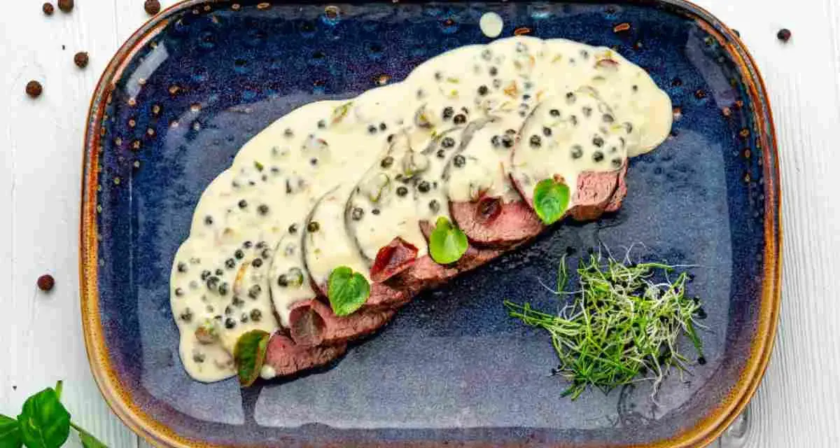 Fette fettine di filetto al pepe verde, ricoperte da una cremosa salsa, guarnite con germogli freschi e foglie verdi.