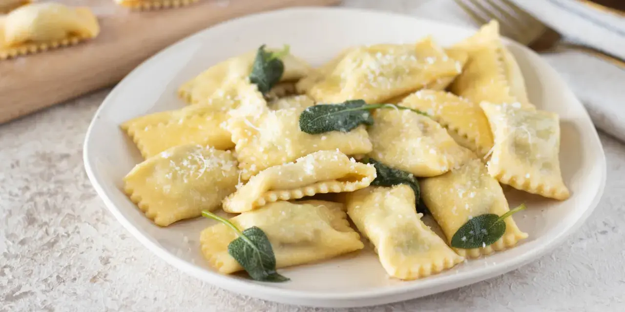 Piatto di ravioli del plin, dorati e spolverati di parmigiano, guarniti con foglie di salvia fresca.