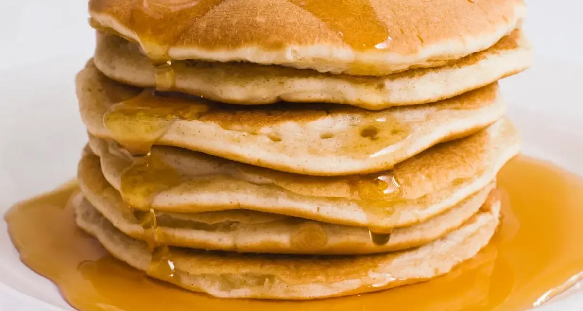 Pila di pancake dorati, inzuppati di sciroppo d'acero. Perfetti per una ricetta pancake proteici sana e golosa.