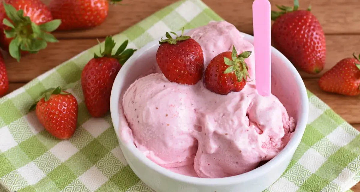 Una ciotola di cremoso gelato alla fragola, guarnito con fragole fresche, su una tovaglietta a quadri verdi.