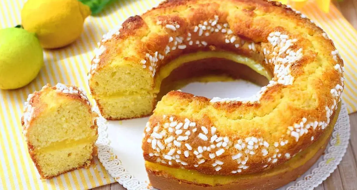 Un soffice ciambellone al limone, decorato con perline di zucchero, con una fetta tagliata che rivela un ripieno cremoso.