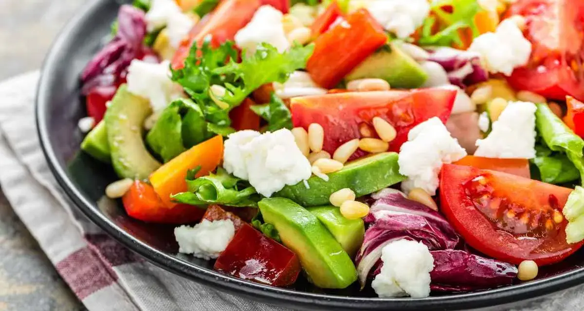 Insalata fresca con pomodori, lattuga, formaggio e avocado a fette, guarnita con pinoli.