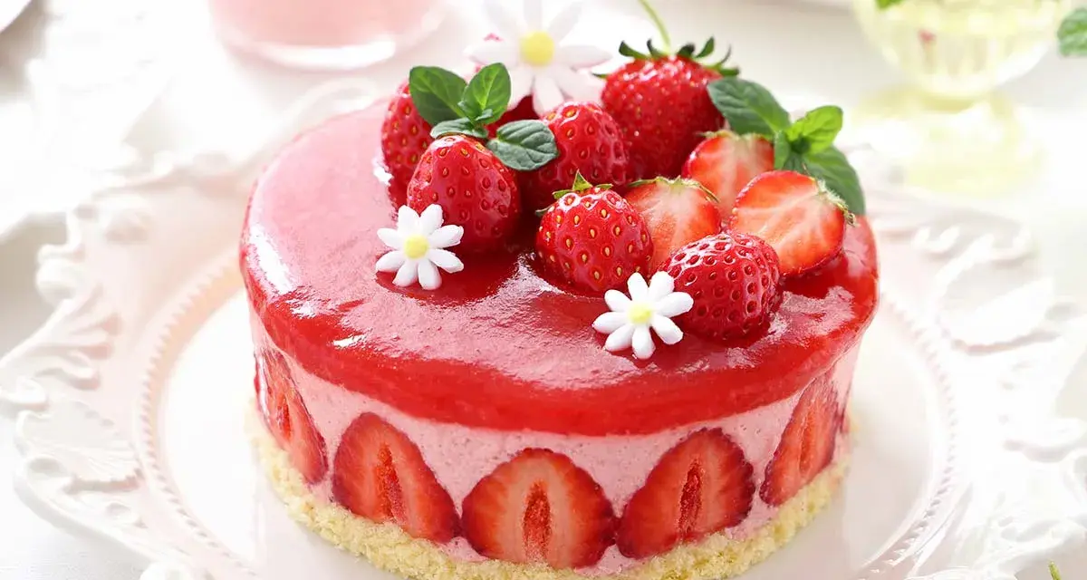 Deliziosa bavarese alle fragole, ricoperta da una gelatina rossa brillante e decorata con fragole fresche, menta e fiorellini bianchi.