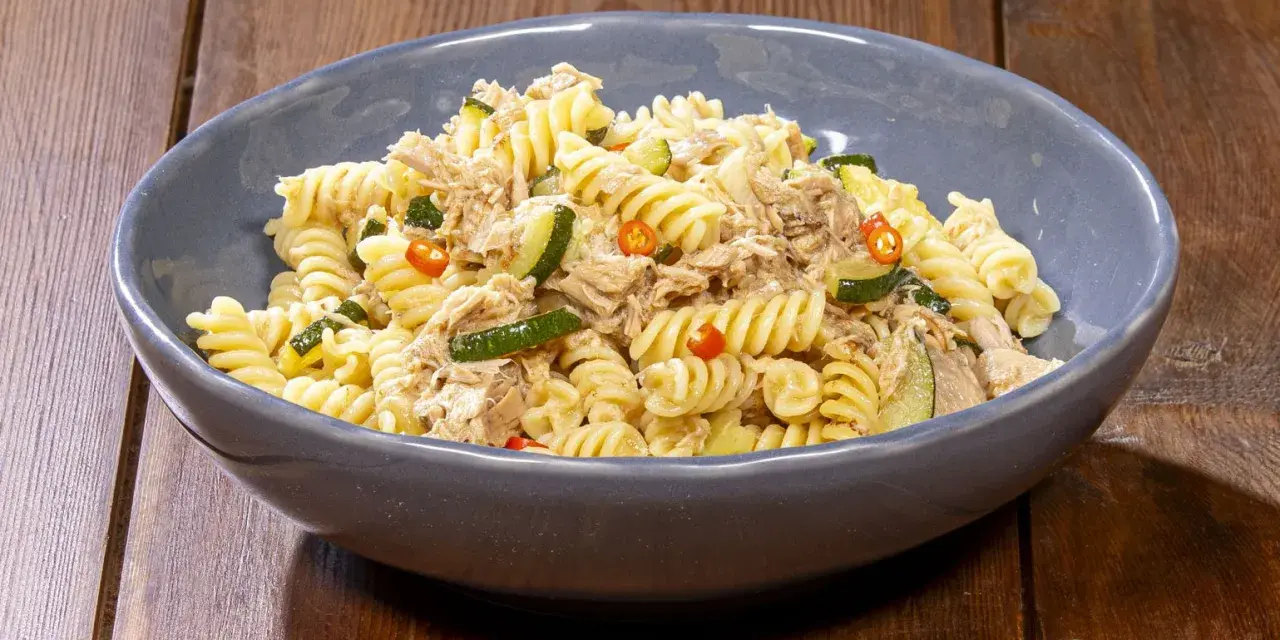 Fusilli con zucchine, tonno e peperoncino in una ciotola blu su un tavolo di legno. Un piatto semplice e gustoso.