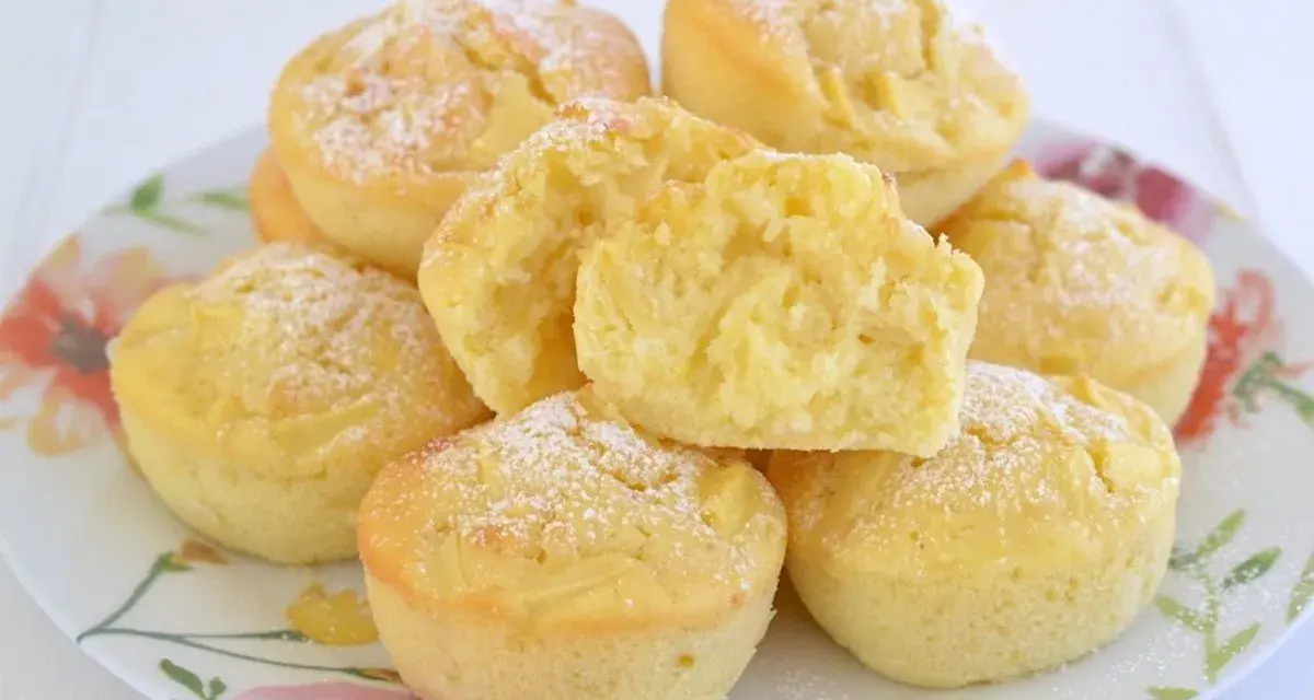 Morbidi muffin alle mele, spolverati di zucchero a velo, su un piatto fiorito. Uno è tagliato a metà, mostrando la soffice mollica.