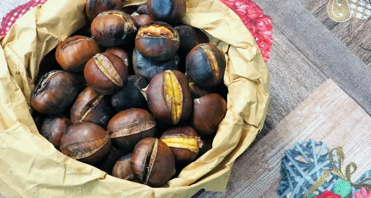 Castagne in friggitrice ad aria, pronte per essere gustate. Un sacchetto di carta marrone trabocca di castagne calde e dorate, alcune con tagli che rivelano il loro interno morbido.