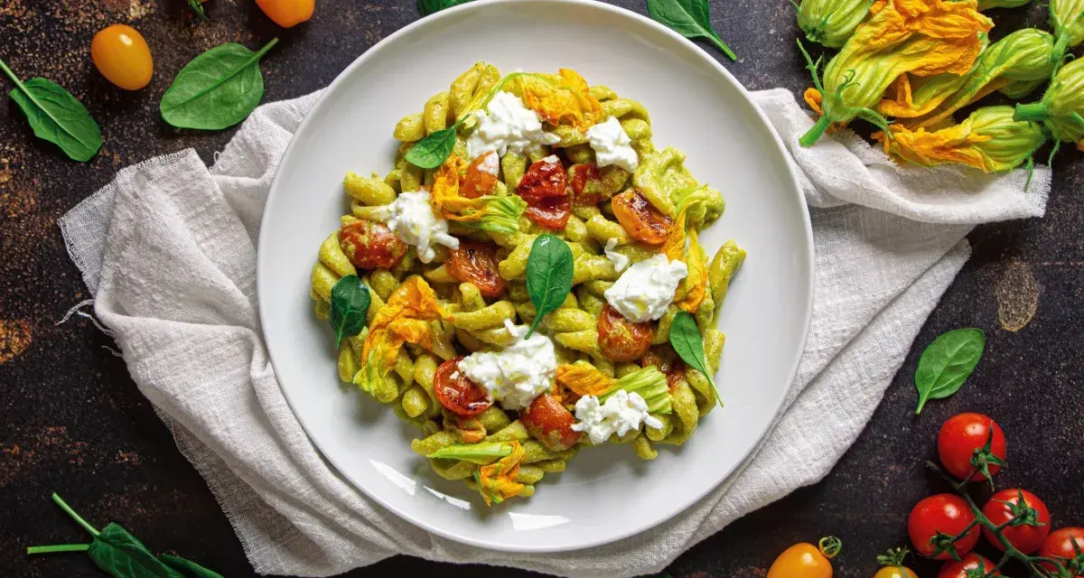 Piatto di pasta con crema di zucchine, pomodorini confit, fiori di zucca e ricotta fresca. Un tripudio di sapori estivi.
