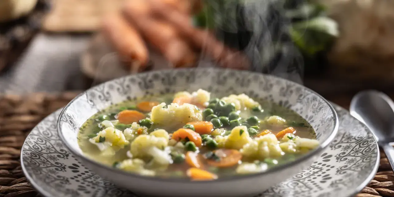 Zuppa fumante con cavolfiore, piselli e carote, arricchita da un tocco di panna da cucina per una cremosità avvolgente.