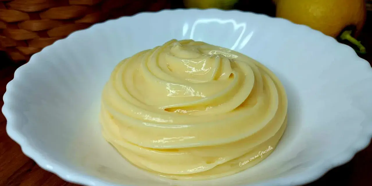 Una spirale di soffice crema al limone in una ciotola bianca, con limoni e uova sullo sfondo.