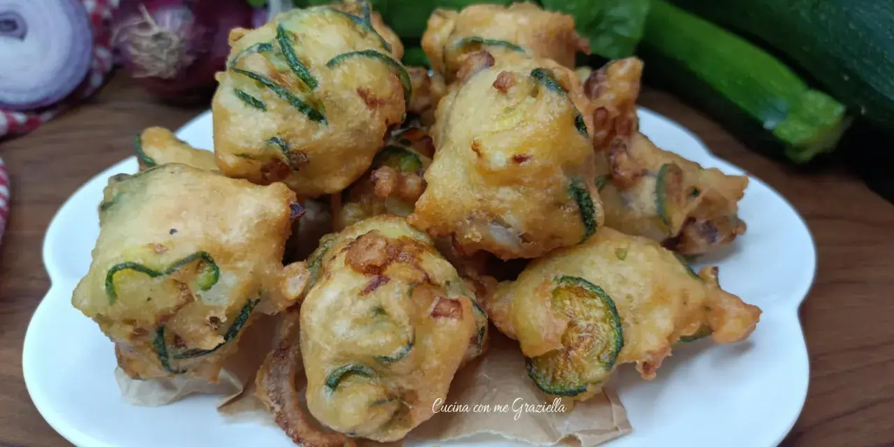 Frittelle di zucchine dorate e croccanti, pronte per essere gustate. Sullo sfondo, cipolle rosse, basilico fresco e zucchine.