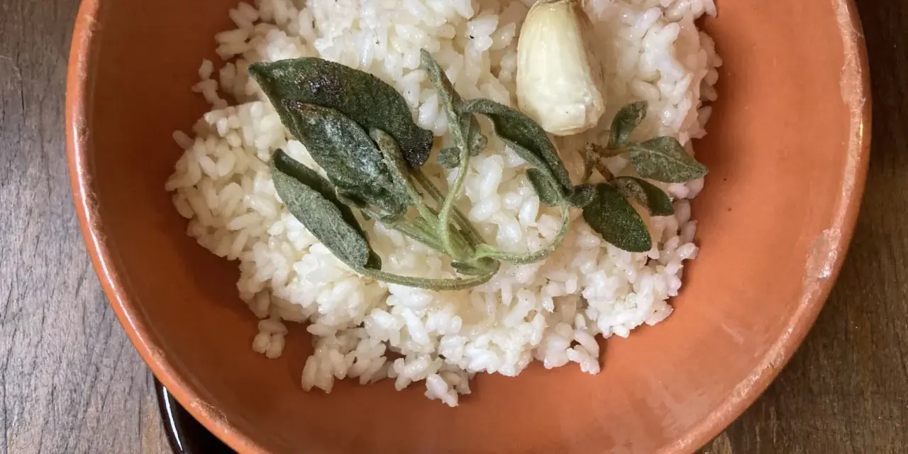 Riso in cagnone, profumato con aglio e salvia croccante, servito in una ciotola di terracotta.