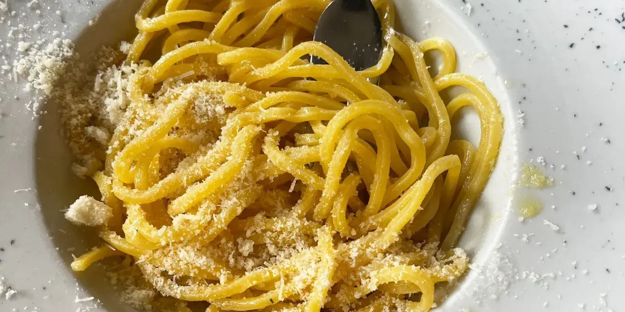 Un piatto di pasta in bianco, spaghetti conditi con formaggio grattugiato e un filo d'olio, pronti per essere gustati.