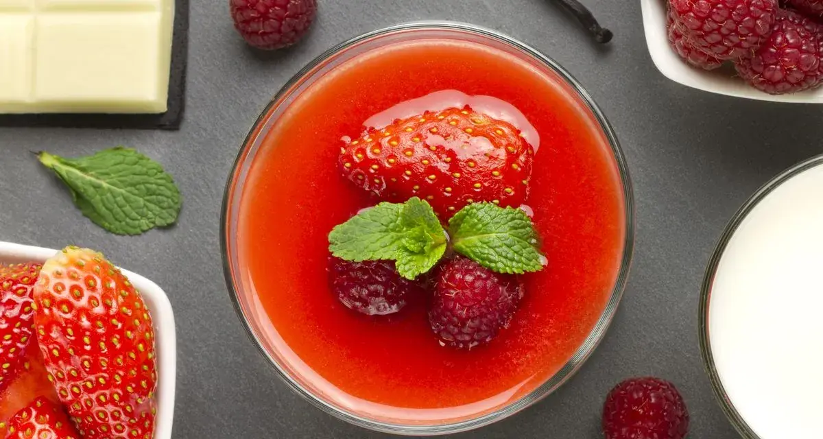 Delizioso coulis di fragole guarnito con fragola, lamponi e menta. Accanto, cioccolato bianco, lamponi freschi e un bicchiere di latte.
