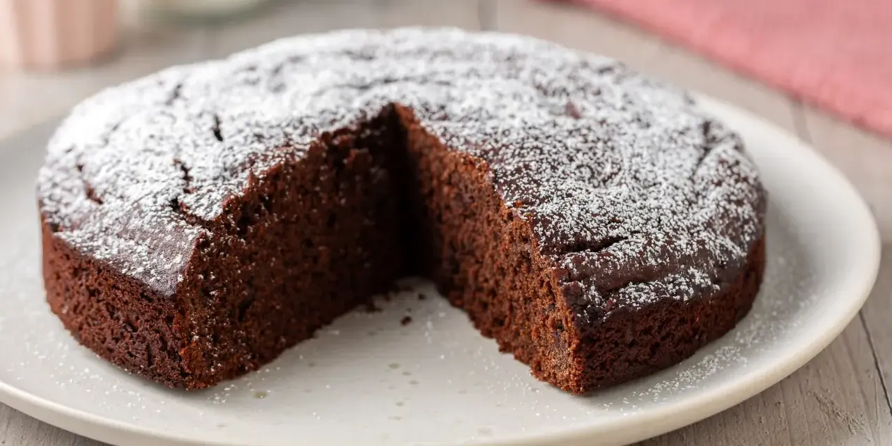 Una fetta è stata tolta da questa torta al cioccolato morbida, cosparsa di zucchero a velo.