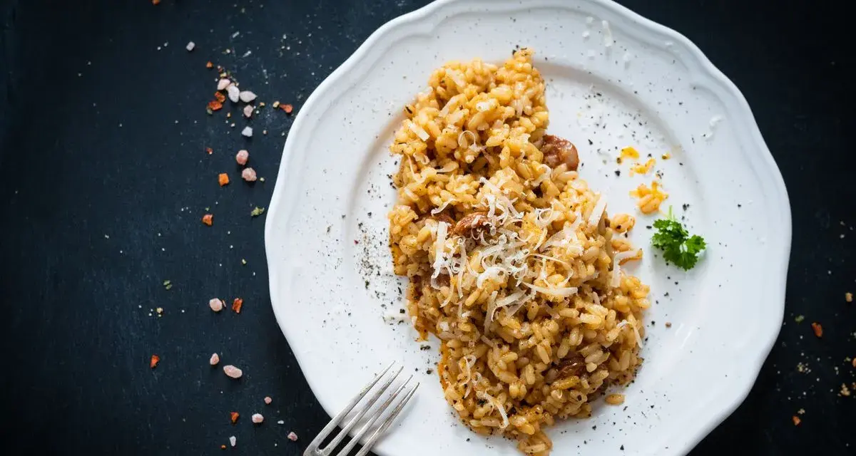 Un piatto di risotto funghi e salsiccia, guarnito con parmigiano grattugiato e prezzemolo, pronto per essere gustato.
