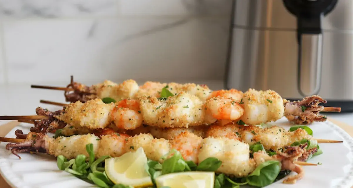 Spiedini di gamberi e calamari dorati e croccanti, cotti alla perfezione nella friggitrice ad aria. Serviti su un letto di insalata con spicchi di limone.