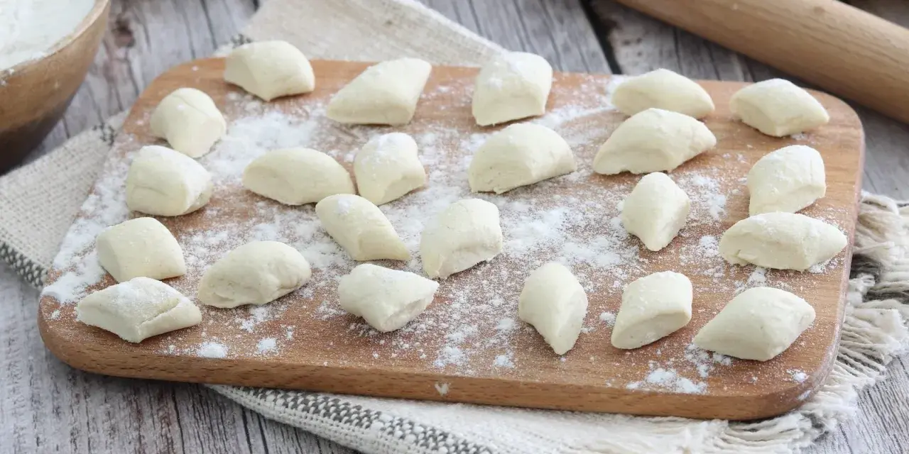 Gnocchi di ricotta freschi, pronti per essere cotti, spolverati di farina su un tagliere di legno.