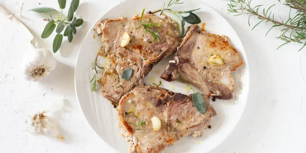 Tre succulente braciole di maiale cotte alla perfezione, guarnite con aglio, rosmarino e salvia.