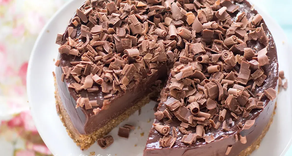 Cheesecake alla Nutella golosa, ricoperta di riccioli di cioccolato fondente. Una fetta è già stata servita, invitando a gustarla.