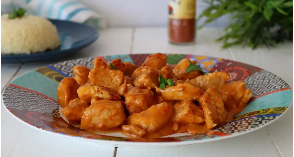 Succulento pollo alla paprika in una salsa cremosa, servito su un piatto colorato con riso bianco sullo sfondo.