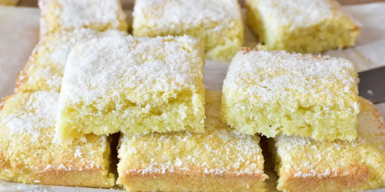 Fette di torta al cocco, soffici e dorate, cosparse di scaglie bianche. Un dolce profumato e invitante.