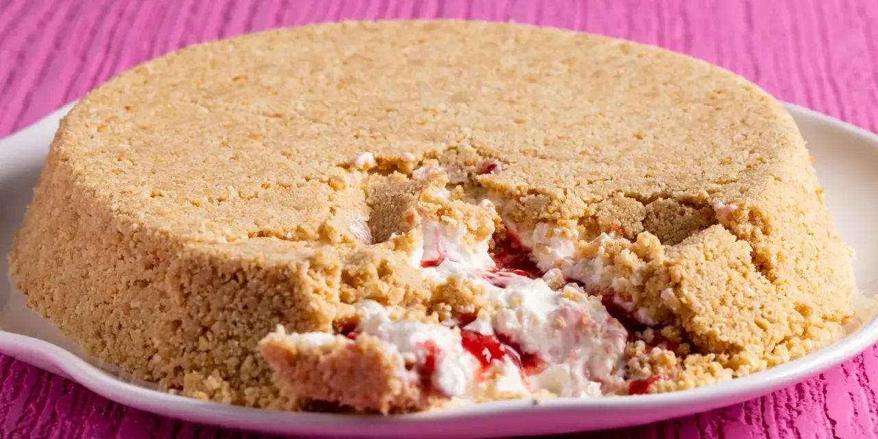 Cheesecake con yogurt greco e marmellata di fragole, con una crosta friabile di biscotti. Un morso goloso rivela il ripieno cremoso.