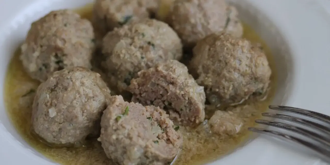 Polpette in umido, morbide e succulente, servite in un piatto bianco con un sughetto invitante.