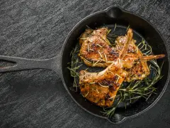 Tre succulenti costolette di agnello in padella, guarnite con rosmarino fresco, pronte per essere gustate.
