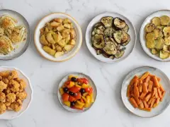 Sette piatti di verdure in friggitrice ad aria: finocchi gratinati, patate arrosto, melanzane, zucchine, cavolfiore fritto, peperoni e carote.