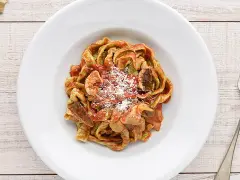 Un piatto di tagliatelle ai funghi, condite con sugo rosso e parmigiano grattugiato, su un tavolo di legno.