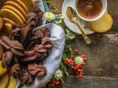Cesto pieno di biscotti fatti in casa al cioccolato e alla vaniglia, accanto a una tazzina di caffè e bacche rosse.