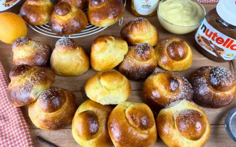 Tanti brioche col tuppo dorati, alcuni spolverati di zucchero a velo, pronti per essere farciti con crema o Nutella.