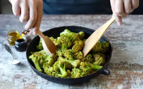 Broccoli in padella, condito con olio e spezie, viene mescolato con due palette di legno.