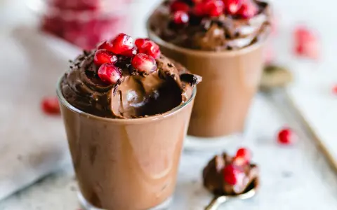 Due bicchierini di golosa mousse al cioccolato, guarniti con chicchi di melagrana e scaglie di cioccolato.