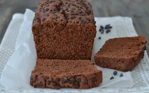 Un soffice plumcake al cioccolato, ricco di gocce, è tagliato a fette su carta da forno.