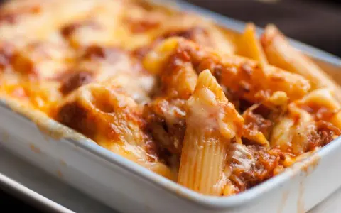 Penne al forno con sugo di pomodoro e mozzarella filante, un classico della pasta alla sorrentina.